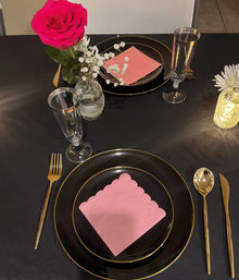 Romantic black-and-gold tablescape with scalloped pink napkin on black plates, gold flatware, champagne flutes, pink rose and baby's-breath centerpiece and a glowing jar light
