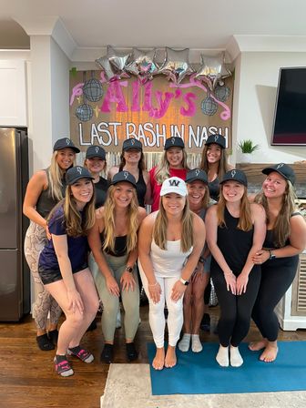 Group of smiling women in matching caps posing in a living room for Ally's 'Last Bash in Nashville' bachelorette party with silver star balloons and disco decor