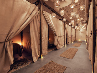Candlelit spa corridor with curtained private treatment pods, wicker pendant lights, and jute rugs for a cozy wellness lounge