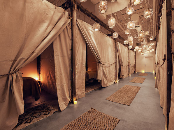Candlelit spa corridor with curtained private treatment pods, wicker pendant lights, and jute rugs for a cozy wellness lounge