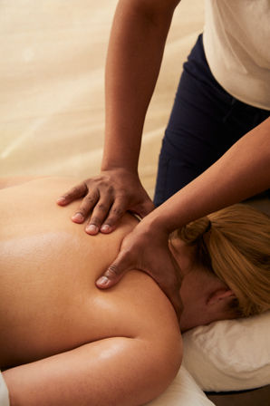 Close-up of a massage therapist’s hands applying firm shoulder and upper-back pressure to a client on a spa table — relaxing massage therapy treatment.