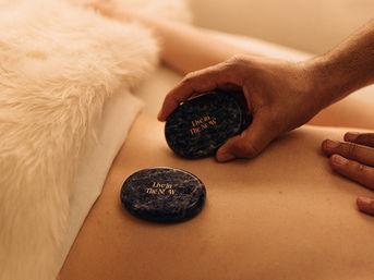 Close-up of hands placing dark polished stones with gold lettering on a client's bare back during a relaxing hot-stone massage on a cozy spa table