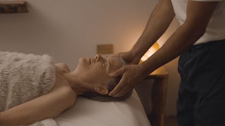 Person lying on a spa table wrapped in a plush blanket while a therapist gives a soothing head massage in a softly lit treatment room