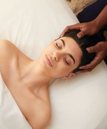 Relaxing scalp massage at a spa — person with eyes closed on a white massage table while therapist’s hands gently cradle and massage the head, a calming wellness treatment.