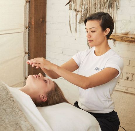 Spa therapist performing a Reiki energy-healing session over a client lying on a treatment table in a cozy wellness studio, relaxation therapy setting.