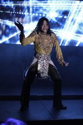 Costumed pop performer in a glittering gold top and jeweled sash striking a dynamic dance pose on a dark stage with bright blue LED light beams