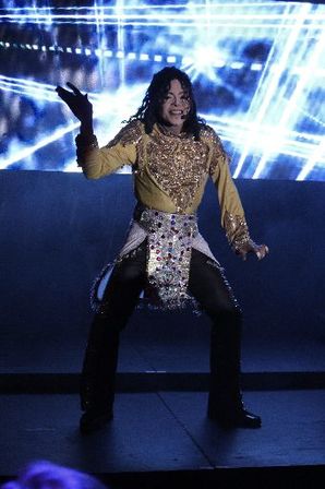 Stage performer in a glittering gold jacket and jeweled belt striking a dynamic dance pose on an indoor concert stage with blue laser-like light visuals