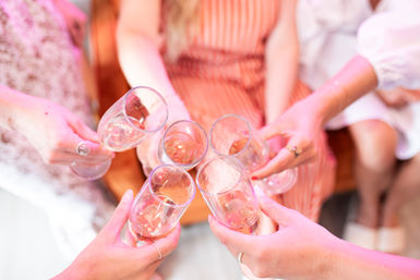 Close-up of friends toasting with champagne flutes under warm pink lighting at an indoor celebration