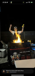 Nighttime outdoor hibachi chef performing a teppanyaki-style flame show on a portable grill cart, mustard bottle raised, condiments and coolers on a patio in Santa Rosa.