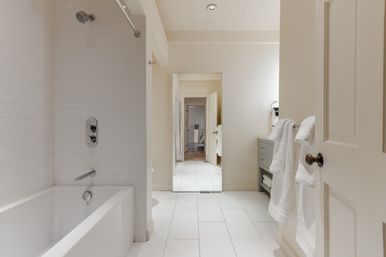 Bright modern bathroom interior with white subway-tile shower and bathtub, chrome showerhead and faucet, white tile floor, gray vanity and neatly folded white towels for a clean, spa-like feel