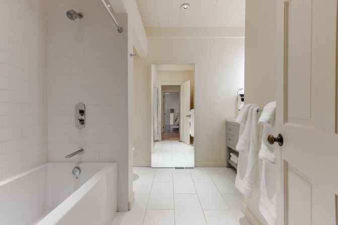 Bright modern bathroom interior with white subway-tile shower and bathtub, chrome showerhead and faucet, white tile floor, gray vanity and neatly folded white towels for a clean, spa-like feel