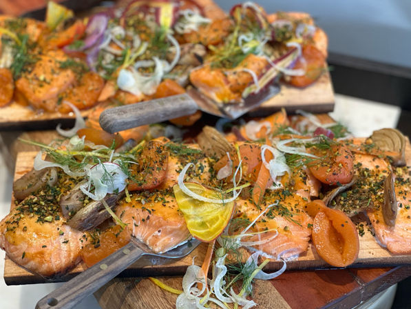 Close-up of planked grilled salmon fillets on wooden serving boards, garnished with roasted apricots, fennel ribbons, fresh herbs and crushed pistachios — vibrant gourmet seafood platter.
