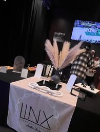Indoor Austin, Texas pop-up vendor table with pampas grass centerpiece, modern jewelry displays on a white tablecloth and a TV showing a basketball game.