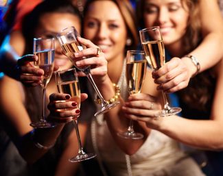 Close-up of friends toasting with champagne flutes at a lively indoor party, bubbling sparkling wine and smiling faces blurred in the background.