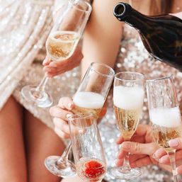 Close-up of champagne flutes clinking at a festive celebration, sparkling bubbly with foam rising and a strawberry in one glass.