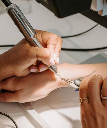 Close-up in a jewelry studio: artisan hands using a rotary tool and pliers to repair a delicate gold chain bracelet on a wrist.