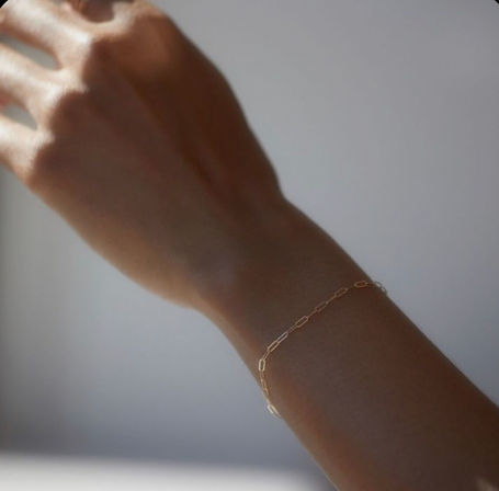 Close-up of a delicate gold paperclip chain bracelet on a wrist, minimalist jewelry photographed in soft natural light