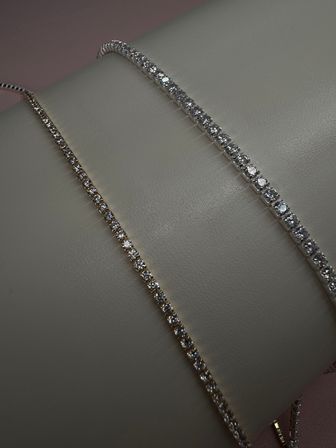 Close-up of two sparkling tennis bracelets with round clear gemstones on a light leather jewelry display, luxury jewelry product shot