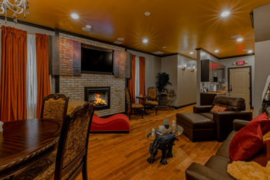 Cozy lounge interior with roaring brick fireplace, wall-mounted TV, leather seating, hardwood floors and warm orange curtains.