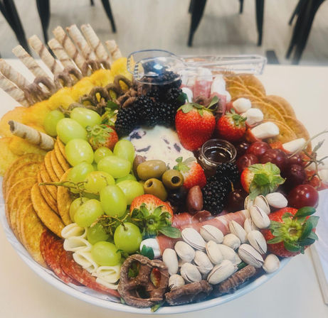 Vibrant charcuterie platter: green and red grapes, strawberries, blackberries, olives, pistachios, crackers and wafer sticks, rolled cheeses and salami, chocolate-covered pretzels and a small jar of jam — colorful grazing bowl for parties