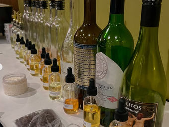 Row of wine bottles and small dropper vials filled with golden aroma samples on a white tablecloth — organized wine-tasting aroma station with jars and sample packets.