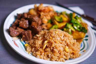 Close-up of a hearty Asian-style dinner plate: golden egg fried rice, seared beef cubes and broccoli stir-fry on a patterned ceramic plate.