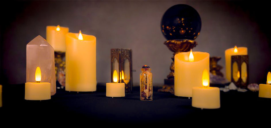 Dimly lit spiritual altar with glowing pillar and tealight candles, a rose quartz point, small potion vial, and a black crystal ball on a dark tabletop — cozy mystic ritual scene
