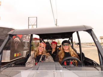 Three smiling women wearing bandanas and harnesses seated in an off-road UTV side-by-side at an outdoor adventure park, ready for a desert trail ride.