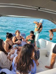 Friends on a sunlit motorboat over turquoise coastal waters, sipping drinks and snapping photos under a canopy