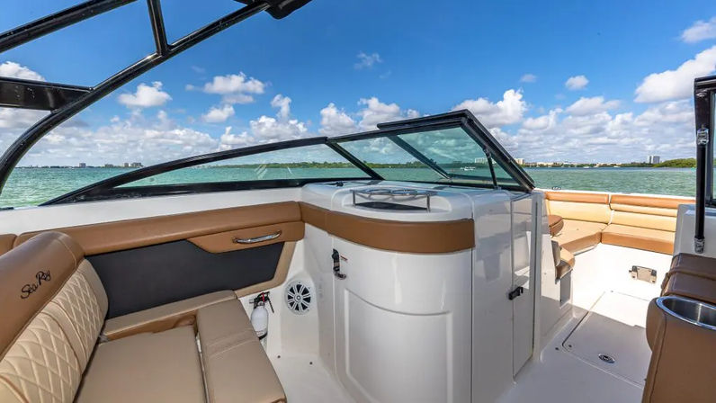 Boat cockpit with tan quilted seating and white fiberglass console, turquoise bay and distant shoreline under a sunny blue sky