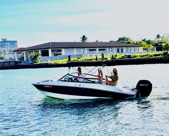 White-and-black motorboat with three people relaxing on a sunny coastal canal cruise past waterfront homes