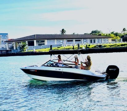White-and-black motorboat with three people relaxing on a sunny coastal canal cruise past waterfront homes