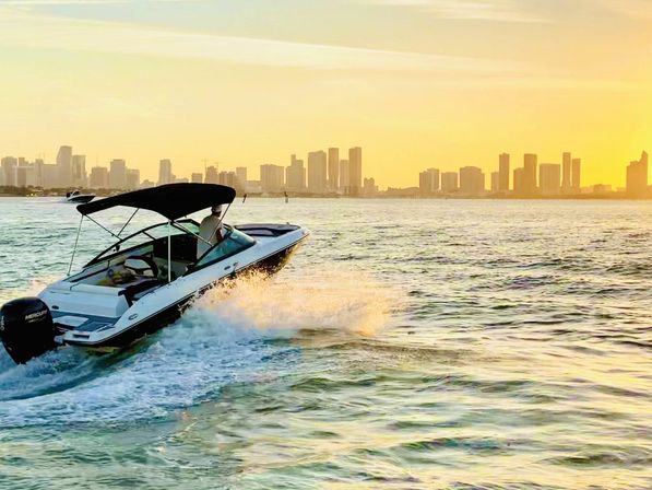 White speedboat skimming turquoise water at golden sunset, spray trailing behind and a modern city skyline on the horizon — urban waterfront boating.