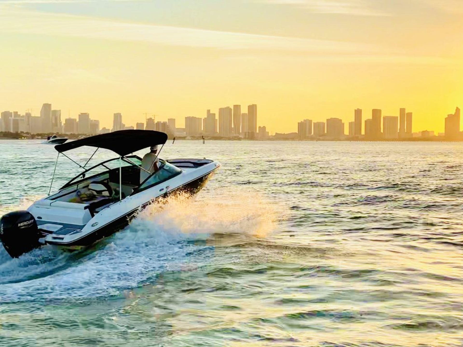 White speedboat skimming turquoise water at golden sunset, spray trailing behind and a modern city skyline on the horizon — urban waterfront boating.