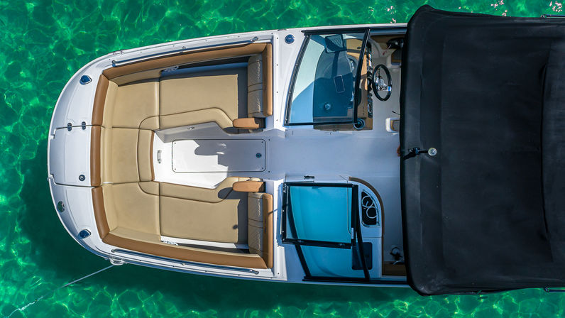Aerial view of a white motorboat with tan cushioned bow seating and a black canopy floating on sparkling turquoise water