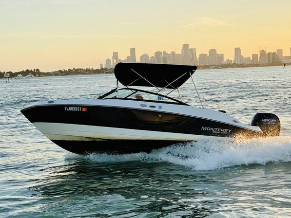 Black-and-white Monterey speedboat skimming choppy water at sunset with a Florida coastal city skyline in the background