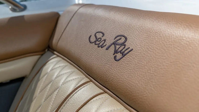 Close-up of tan and cream boat bench seat upholstery—quilted cream cushion with brown piping and an embroidered script logo on tan vinyl.