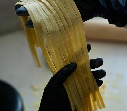 Gloved hands holding long, floured ribbons of freshly cut fettuccine in an artisan kitchen