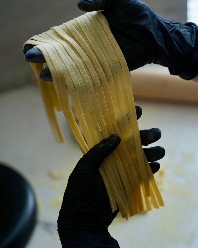 Gloved hands holding long, floured ribbons of freshly cut fettuccine in an artisan kitchen