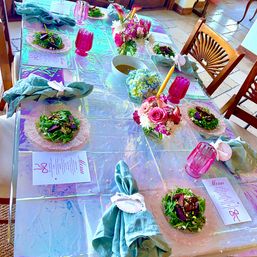 Iridescent indoor tablescape with pastel tablecloth, glass salad plates, green linen napkins, pink goblets, floral centerpieces, candles and printed menus for a festive brunch or dinner.