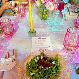 Iridescent bridal brunch table with beet and goat cheese arugula salad on a textured glass plate, pink goblets, yellow taper candle, floral centerpiece and printed menu