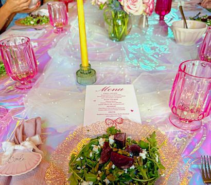 Iridescent bridal brunch table with beet and goat cheese arugula salad on a textured glass plate, pink goblets, yellow taper candle, floral centerpiece and printed menu