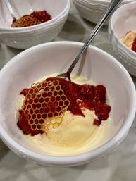 Close-up of creamy vanilla ice cream in a white ceramic bowl topped with vibrant strawberry compote and a decorative honeycomb sugar tuile, with a silver spoon.
