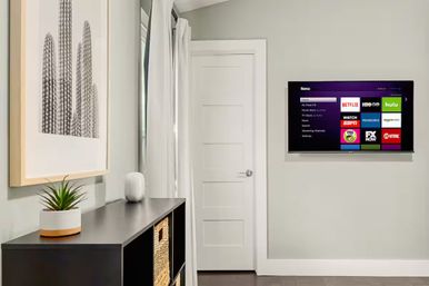 Modern minimalist entryway with wall-mounted smart TV showing streaming app tiles, black console with potted succulent and woven baskets, and framed cactus print