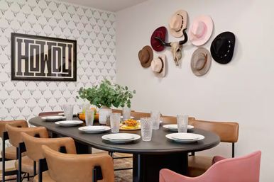 Southwestern-style dining room with black oval table set for eight, leather chairs, 'HOWDY' wall art, cowboy hat and skull display, longhorn-pattern wallpaper and eucalyptus centerpiece.