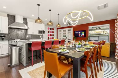 Modern open-concept kitchen and dining room with marble island, red bar stools, pendant lights, dark wood dining table set for eight, yellow sofa and wall-mounted TV