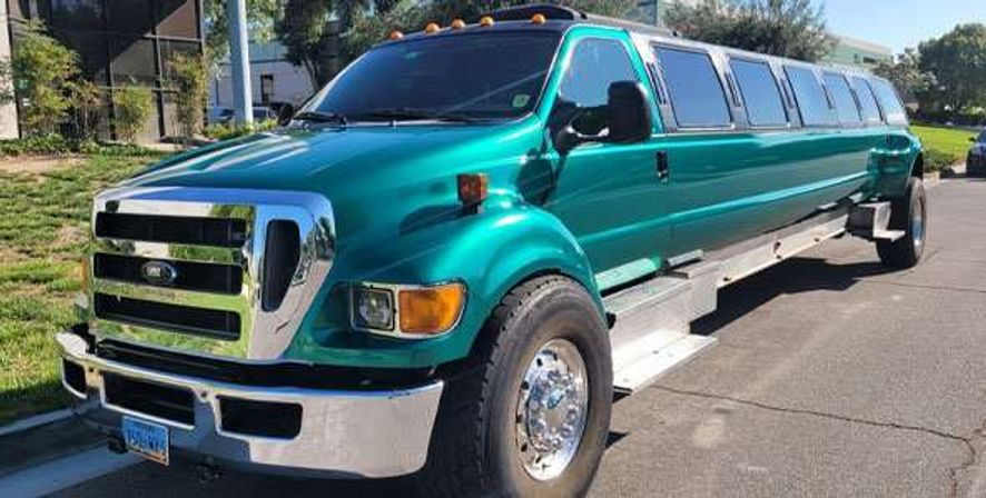 Turquoise-green stretched truck limousine with chrome grille and wheels and a long row of passenger windows, parked on a sunny suburban street.