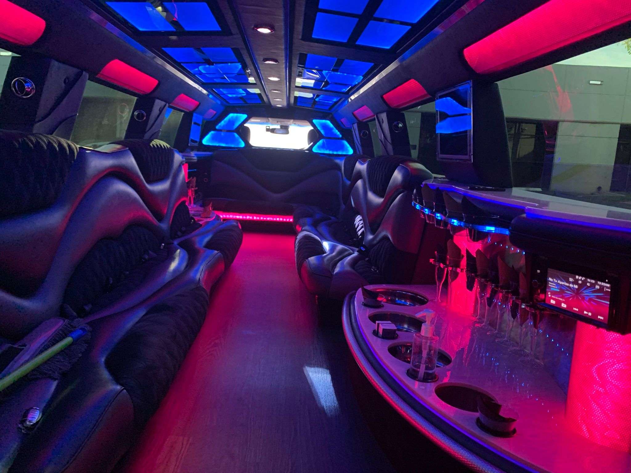 Stretch limousine interior with curved black leather seats, pink and blue LED ambient lighting, glassware bar, cup holders and skylight panels, party-ready