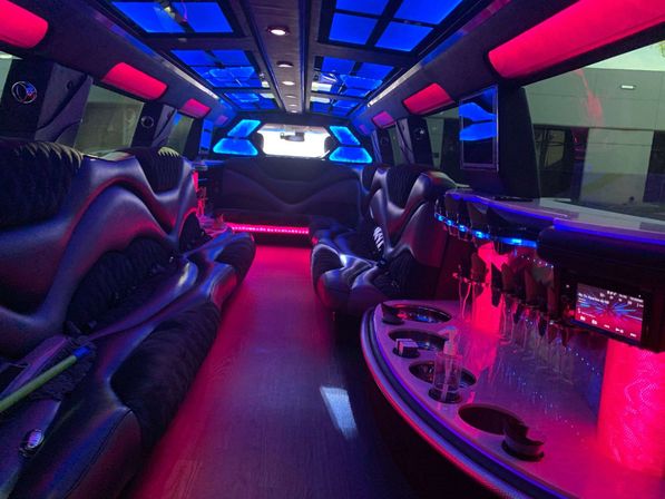Stretch limousine interior with curved black leather seats, pink and blue LED ambient lighting, glassware bar, cup holders and skylight panels, party-ready