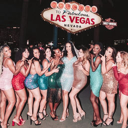 Group of women in colorful sequined party dresses and heels posing under the glowing "Welcome to Fabulous Las Vegas Nevada" sign at night — fun bachelorette-style celebration